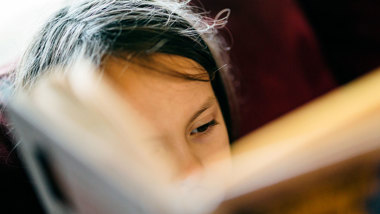 Ett ansikte bakom en uppslagen bok.