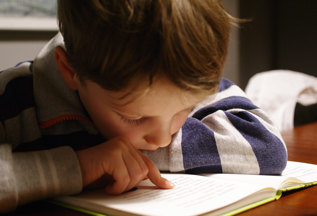 En pojke läser en bok och följer texten med pekfingret.