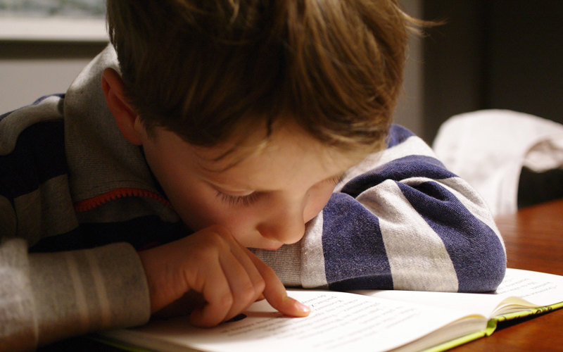 En pojke läser en bok och följer texten med pekfingret.