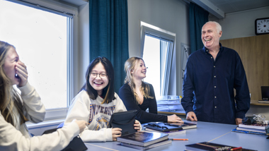 En lärare och tre elever samtalar och skrattar i ett klassrum.