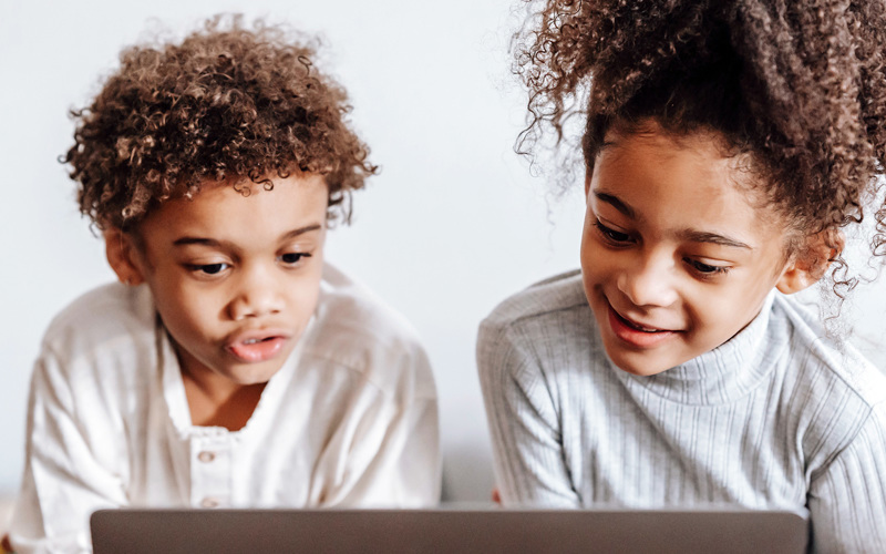 En flicka och en pojke framför en datorskärm.