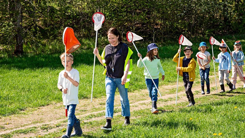 Barn kommer tågande med håvar i luften. Sommardag.