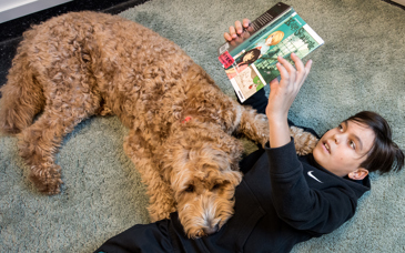 Pojke ligger på golv och läser en bok. Hund ligger bredvid med huvudet på pojkens mage.