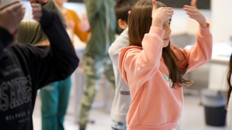Barn står i klassrum och gör rörelse med händerna.