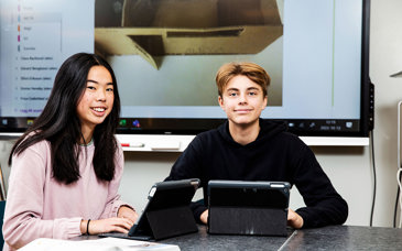 Två glada elever framför dataskärmar.