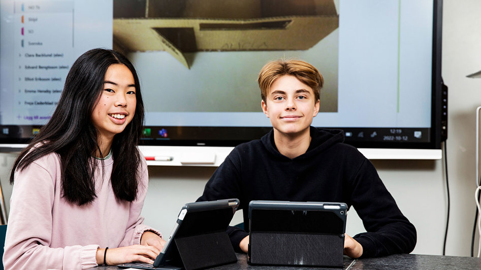 Två glada elever framför dataskärmar.