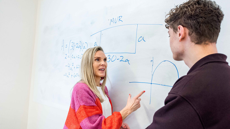 En lärare och en elev står och pratar vid en whiteboard.