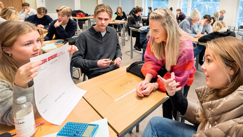 En lärare sitter och diskuterar med elever i ett klassrum.