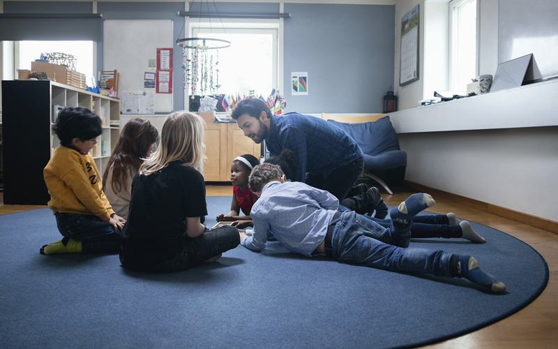 Lärare visar något för barn som sitter runt honom i en cirkel.
