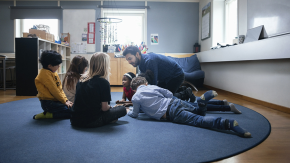 Lärare visar något för barn som sitter runt honom i en cirkel.