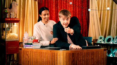 En man står framför en kvinna och tittar rakt fram och pekar framåt. 