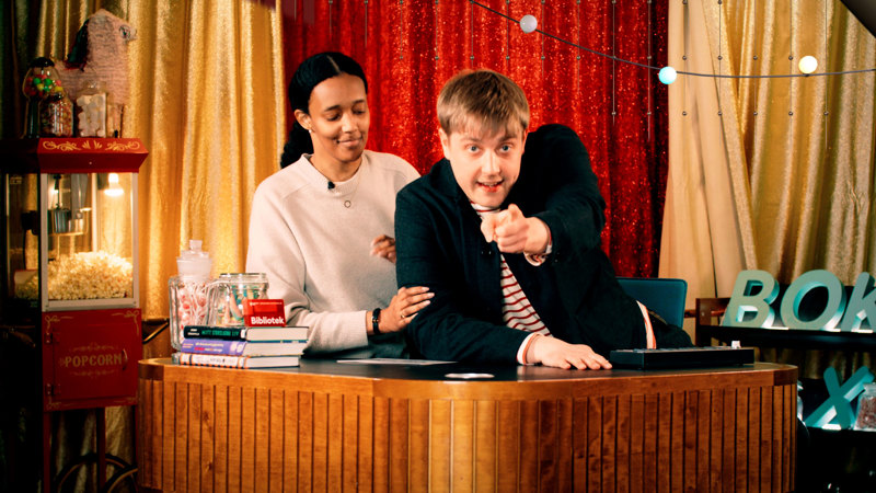 En man står framför en kvinna och tittar rakt fram och pekar framåt. 