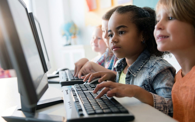 Barn i lågstadieåldern skriver på tangentbord och tittar på skärmen.