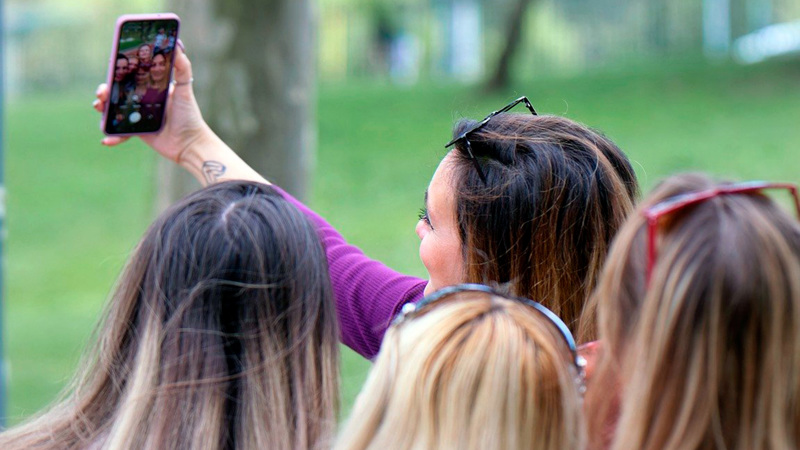 Fyra tjejer tar en selfie med mobiltelefonen utomhus.