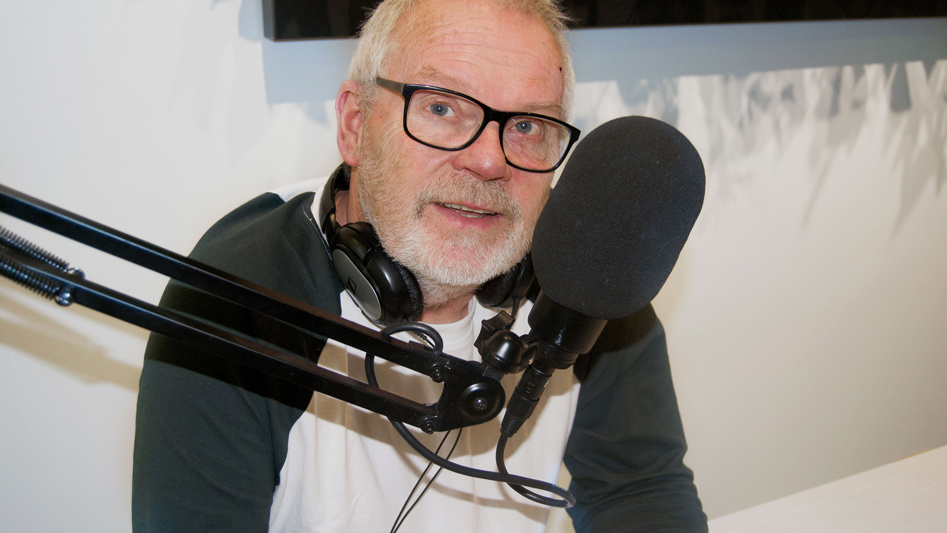 En man med hörlurar sitter vid en mikrofon.