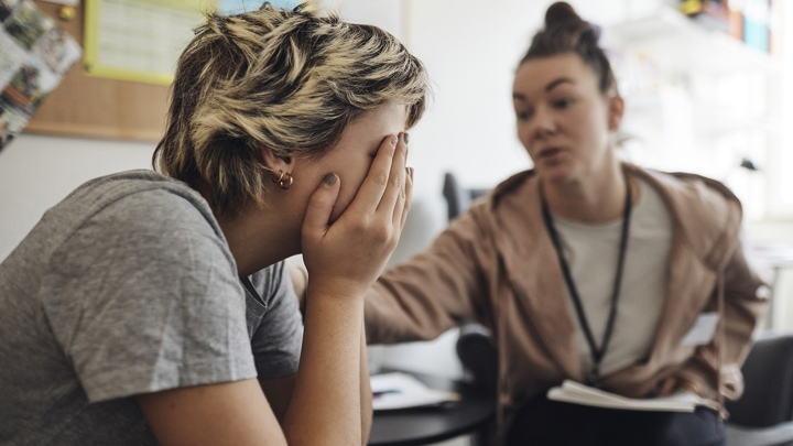 Elev har händerna för ansiktet och blir tröstad av vuxen.