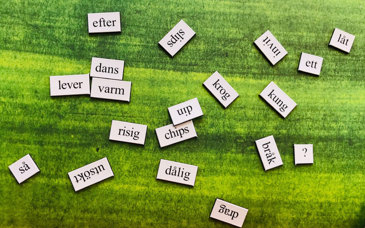 Vita små lappar med ord utspridda på en grön matta.