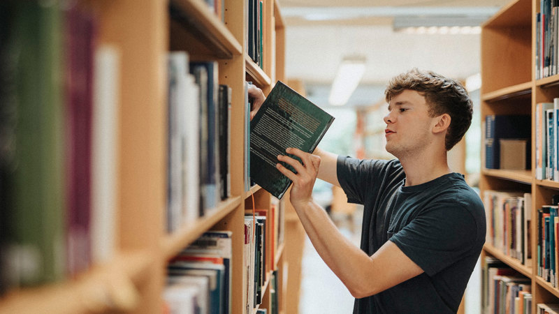 En kille lyfter ut en bok ur en bokhylla i skolbiblioteket.