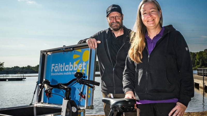 Två personer står vid en lådcykel med Fältlabbets logotype. De ler och tittar in i kameran