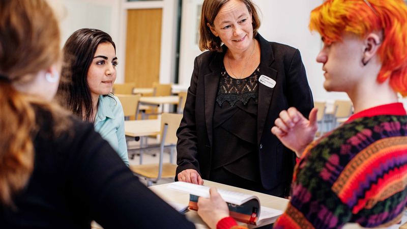 Lärare och tre elever i klassrum. De diskuterar något och ser engagerade ut.