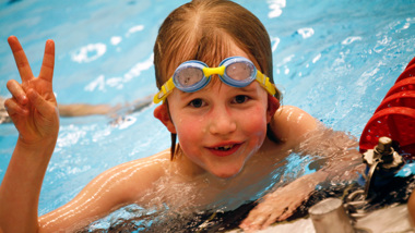 Ett barn med simglasögon i pannan gör ett v-tecken med fingrarna.