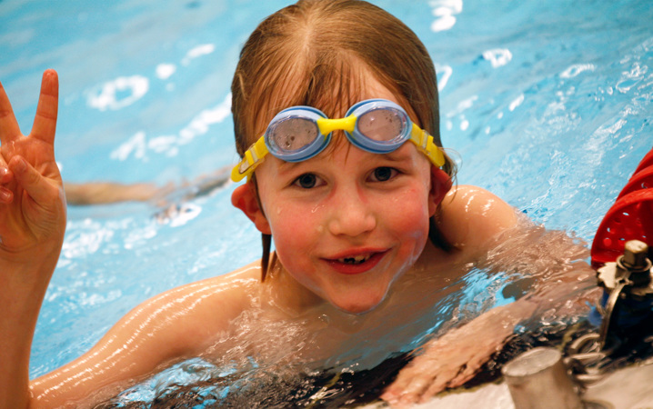 Ett barn med simglasögon i pannan gör ett v-tecken med fingrarna.