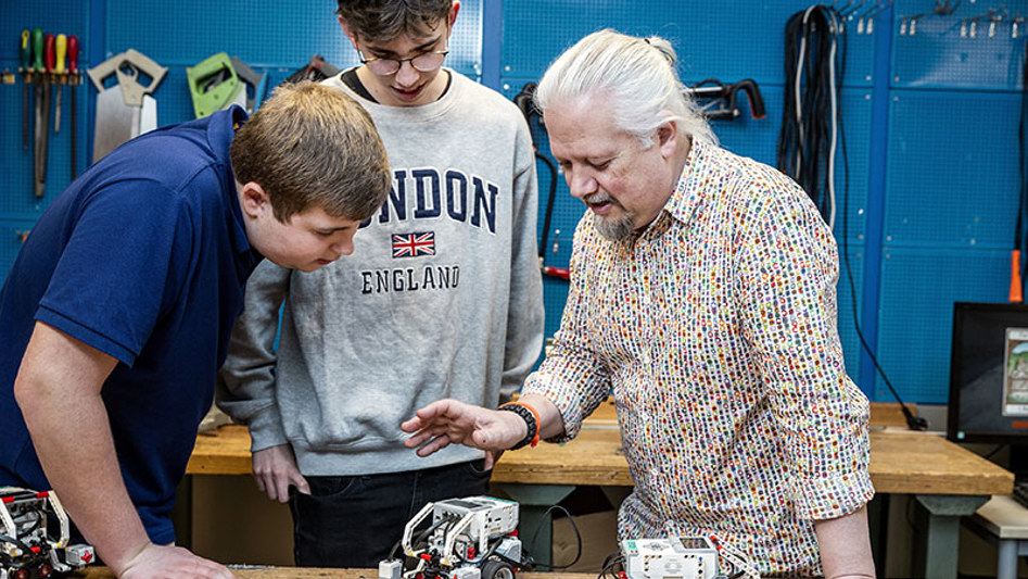 Engagerad lärare och två entusiastiska elever tittar på en robot tillverkad i lego.