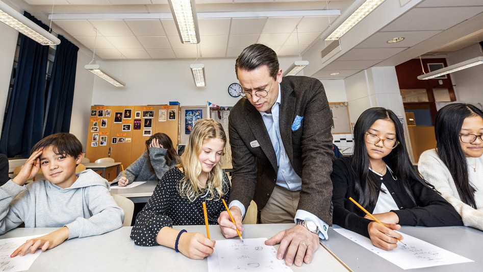 En lärare hjälper en elev vid ett bord med fyra elever.