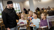 Kökschef tillsammans med glada skolbarn som hämtar mat i matsal.