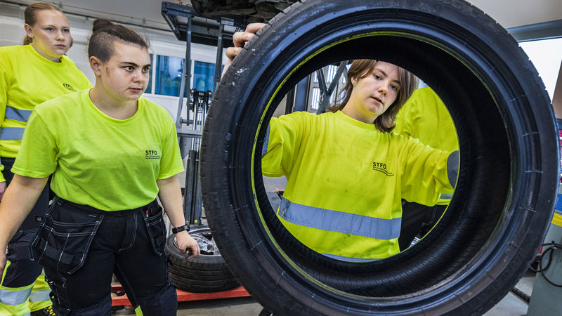 Tre elever i neonfärgade kläder övar på att byta däck.