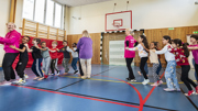 En grupp barn och lärare bildar två led och dansar i en gymnastiksal