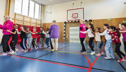 En grupp barn och lärare bildar två led och dansar i en gymnastiksal