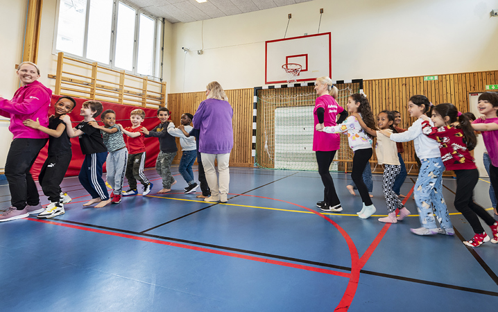 En grupp barn och lärare bildar två led och dansar i en gymnastiksal