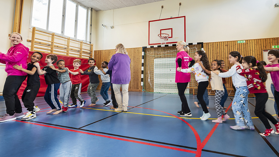 En grupp barn och lärare bildar två led och dansar i en gymnastiksal