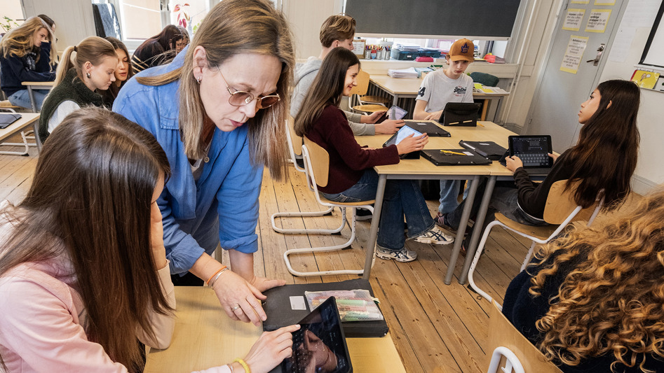 Ett klassrum med elever. En elev och en lärare tittar tillsammans på en Ipad.