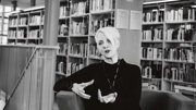 Svarklädd kvinna som sitter i ett bibliotek.