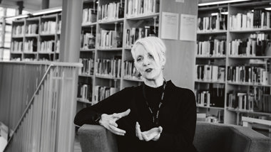 Svarklädd kvinna som sitter i ett bibliotek.