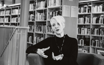 Svarklädd kvinna som sitter i ett bibliotek.