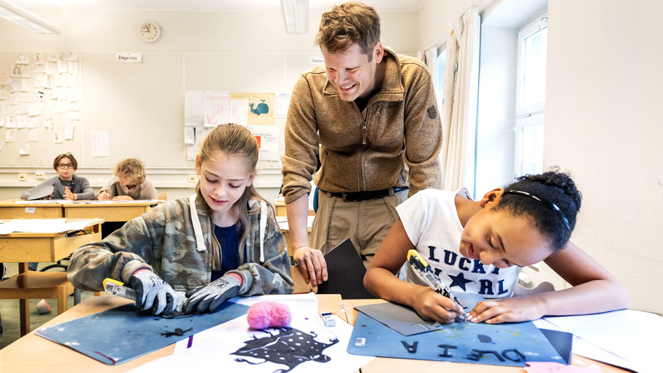Elever skapar konst i klassrum, engagerad lärare tittar på. 