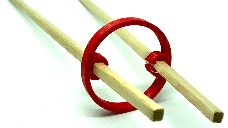 Exempel på teknikutvecklings- och konstruktionsarbete i form av två träpinnar med en röd rund ring.