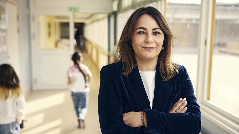 Rektorn Sofia Panagiotidou står i en solig skolkorridor. Två barn syns passera i bakgrunden.
