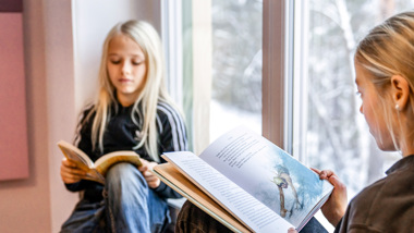 Två flickor sitter i ett fönster och läser.