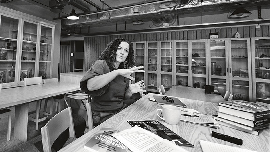 Kvinna som sitter vid bord och berättar något med hjälp av gester. Svartvit bild.