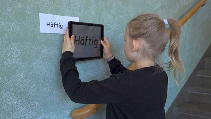 En flicka fotar en lapp på väggen med texten Häftig med sin Ipad.