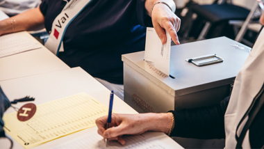 En person lägger en valsedel i en förseglad låda och en annan prickar av på en lista.