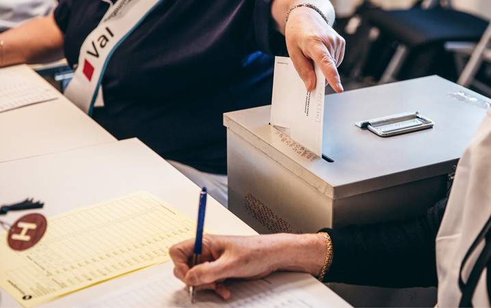En person lägger en valsedel i en förseglad låda och en annan prickar av på en lista.