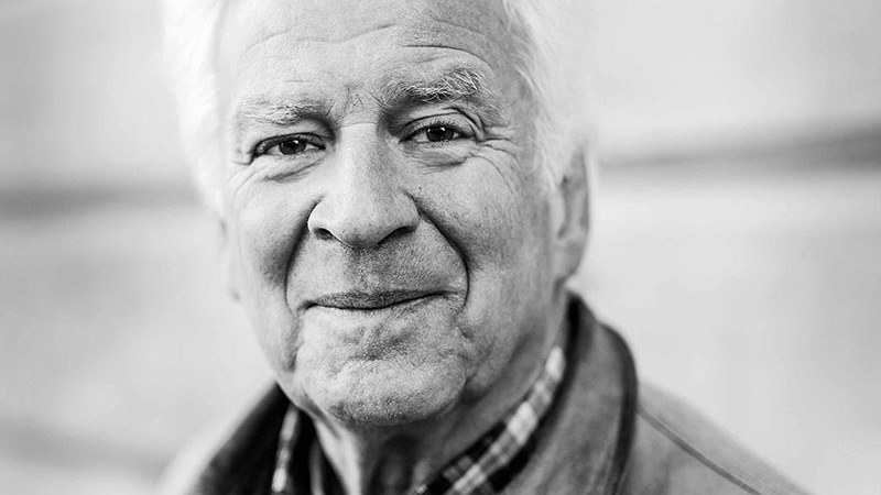 Porträttbild i svartvitt på äldre man som ler. 