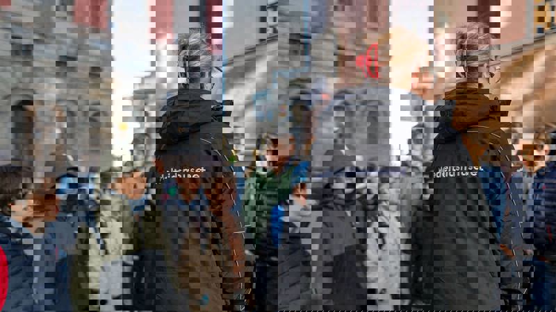 En museipedagog med elever runt sig i stadsmiljö.