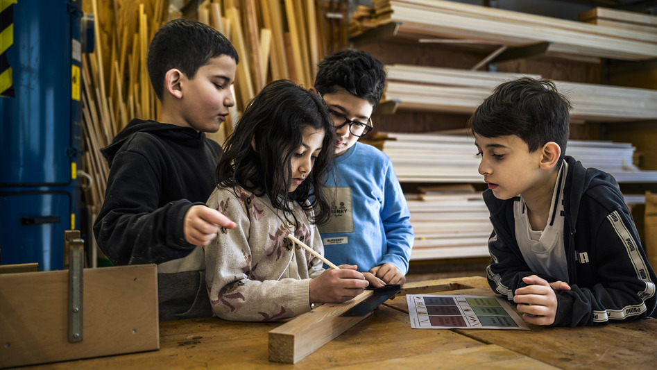 En flicka jobbar med en träbit i en slöjdsal. Tre pojkar står bredvid henne.