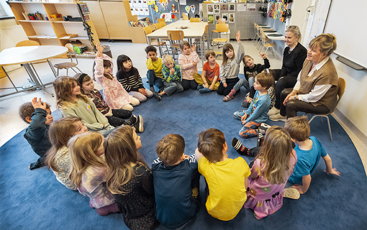 En grupp med barn och lärare sitter i en ring på golvet i ett klassrum.